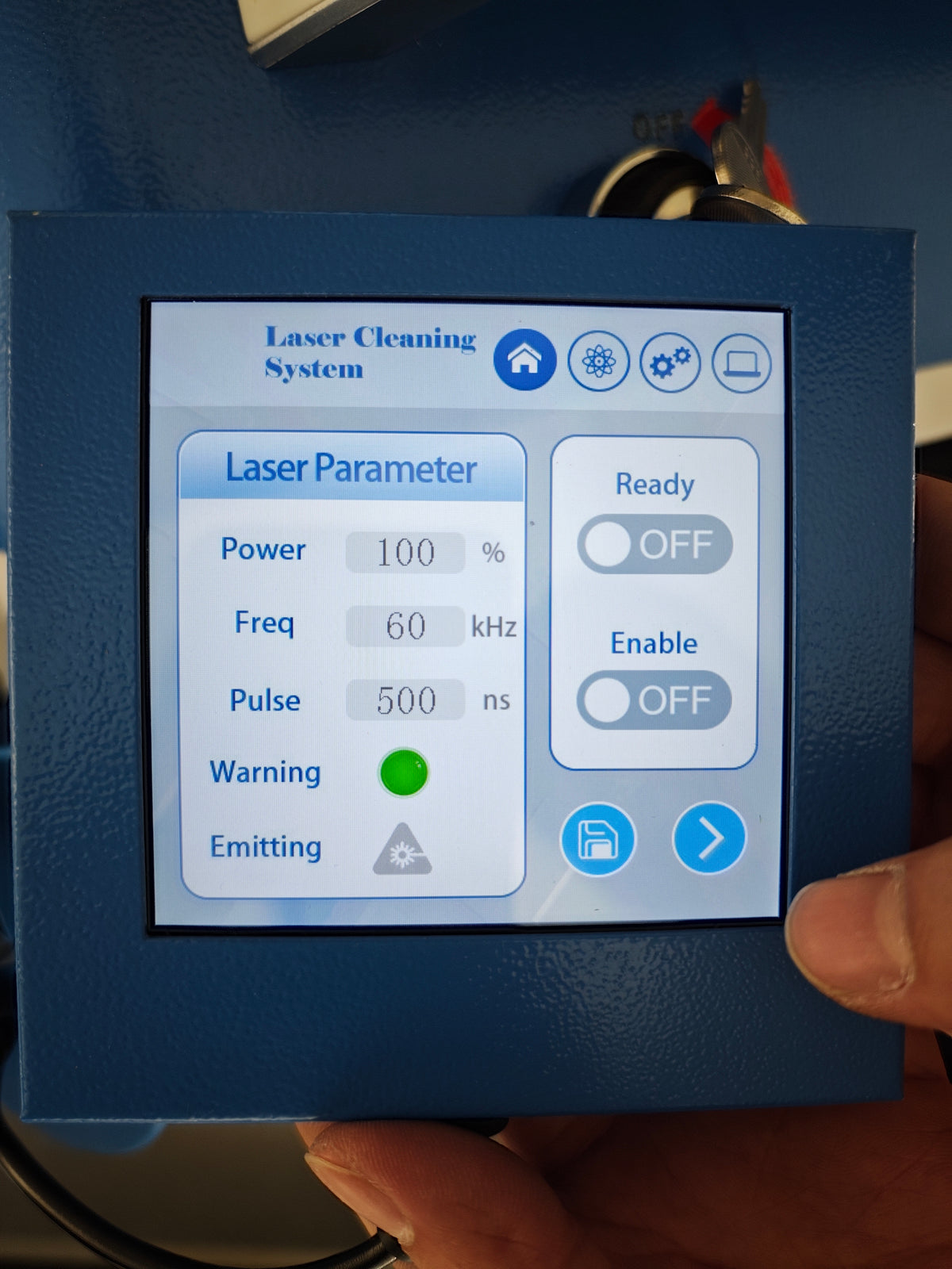A close-up of the handheld laser cleaning system control panel with a digital display screen showing settings like power, frequency, and pulse, held by a hand.