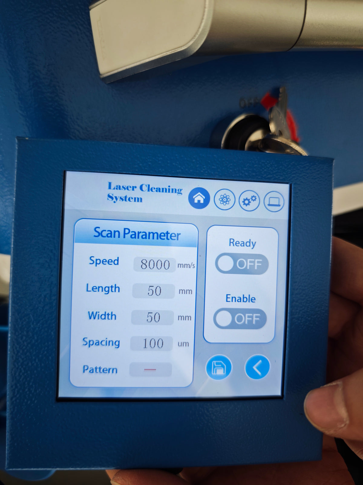 A close-up of the handheld control panel with a touchscreen displaying laser cleaning system settings.