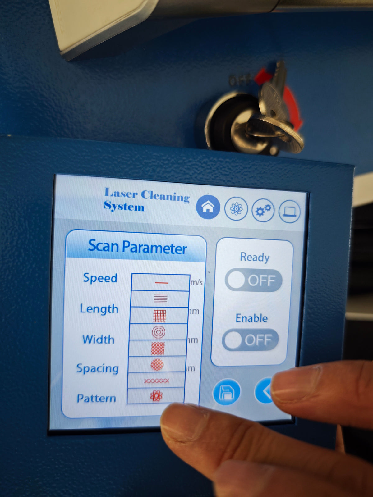 A close-up of the handheld control panel with a touchscreen displaying settings for a laser cleaning system, including speed, length, width, spacing, and pattern. 
